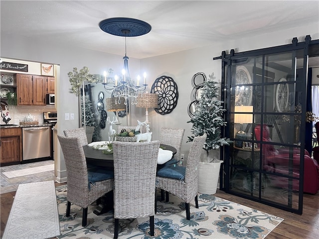 dining room featuring a barn door, an inviting chandelier, and light hardwood / wood-style flooring