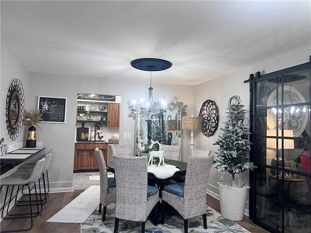 dining space featuring a textured ceiling, dark hardwood / wood-style flooring, a barn door, and an inviting chandelier