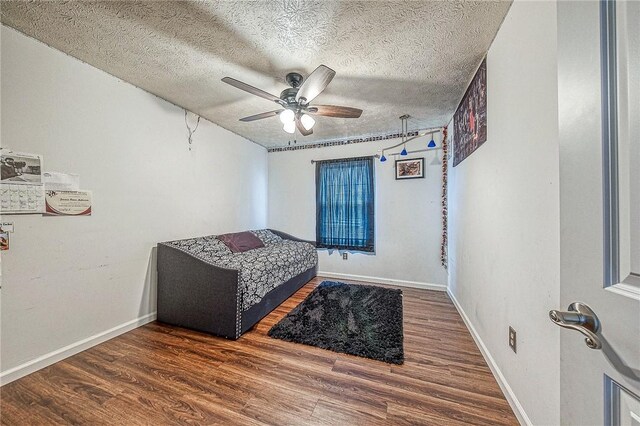 bedroom with a ceiling fan, a textured ceiling, baseboards, and wood finished floors