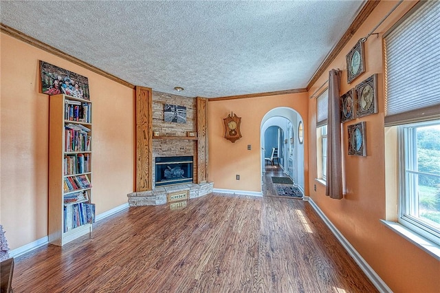 unfurnished living room featuring crown molding, a textured ceiling, wood finished floors, and a stone fireplace