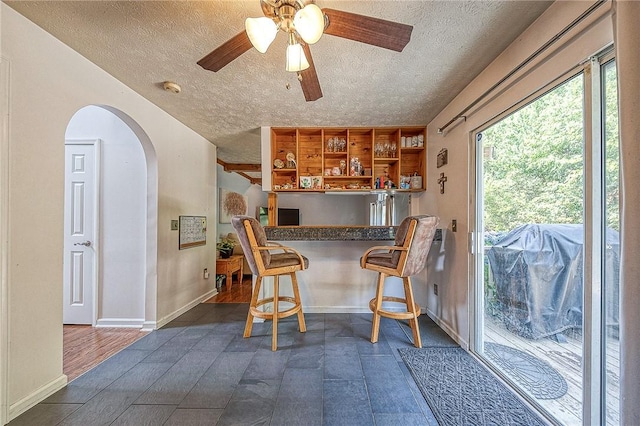 interior space featuring a breakfast bar, dark countertops, arched walkways, and a textured ceiling