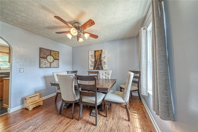 dining area featuring arched walkways, ceiling fan, a textured ceiling, and wood finished floors