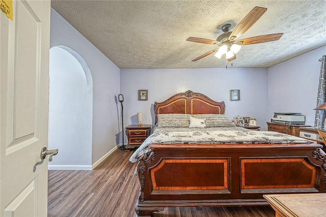 bedroom featuring arched walkways, a textured ceiling, a ceiling fan, baseboards, and dark wood finished floors