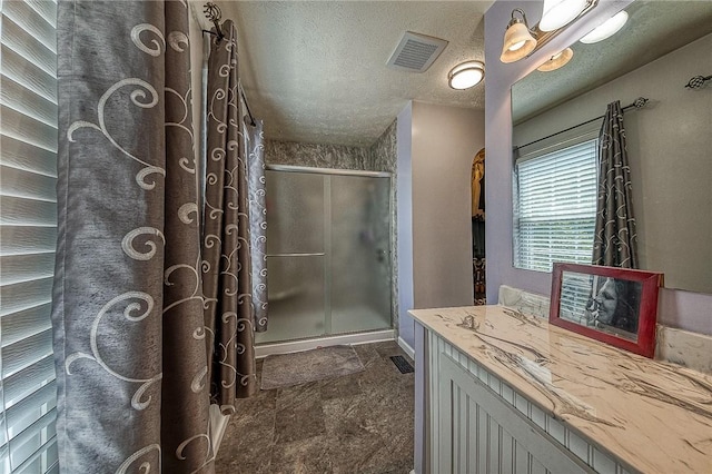 bathroom with visible vents, a shower stall, a textured ceiling, and vanity