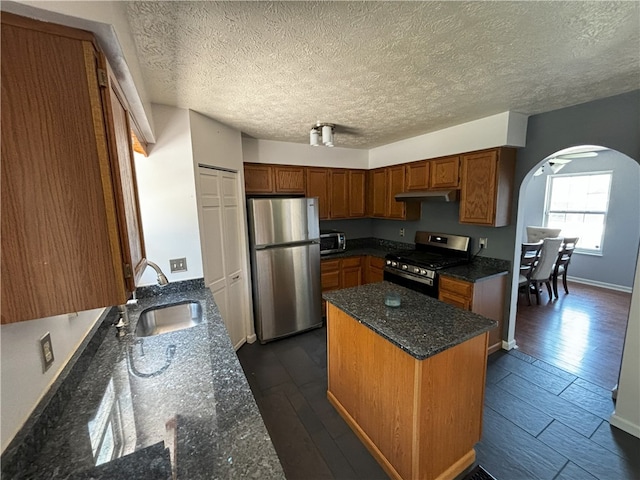 kitchen with arched walkways, under cabinet range hood, a sink, appliances with stainless steel finishes, and a center island