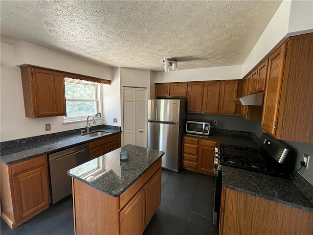 kitchen with appliances with stainless steel finishes, brown cabinetry, a sink, and dark stone counters