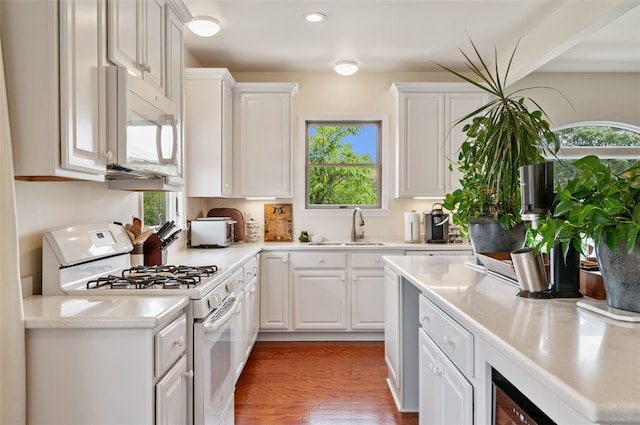 kitchen featuring white appliances, white cabinetry, a wealth of natural light, and a sink