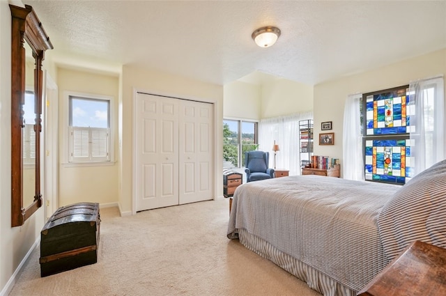 bedroom featuring a closet, light carpet, a textured ceiling, and baseboards