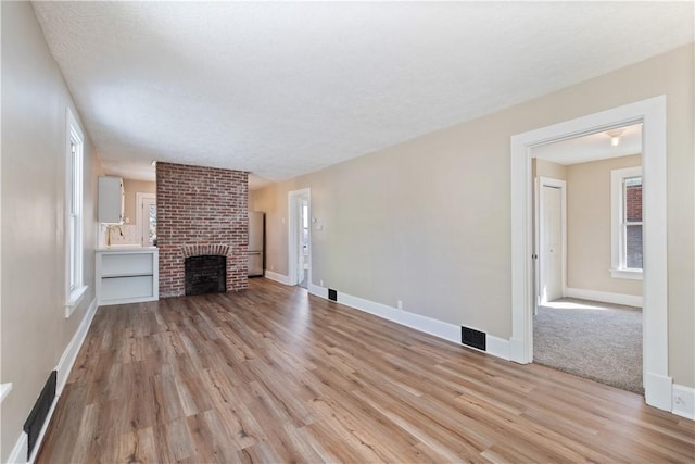 unfurnished living room featuring sink, light wood-type flooring, a textured ceiling, and a brick fireplace