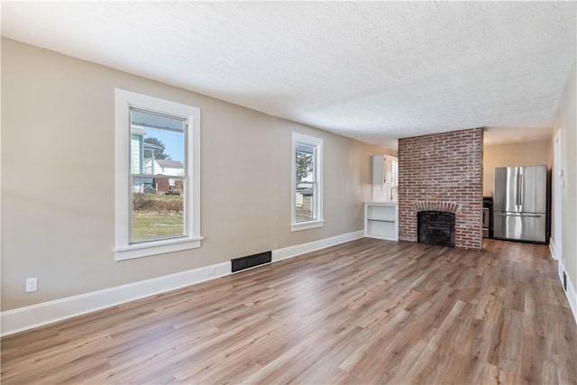 unfurnished living room with a textured ceiling, a fireplace, and light hardwood / wood-style flooring