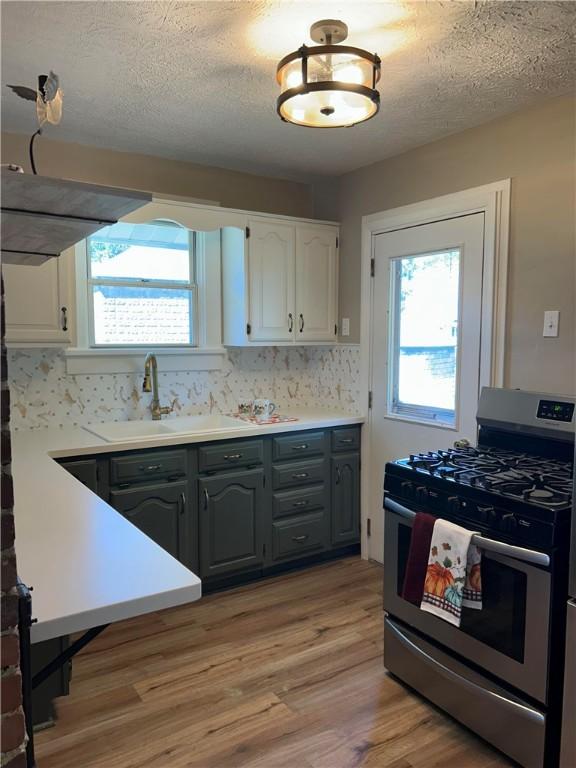 kitchen featuring white cabinets, stainless steel gas stove, gray cabinets, and sink