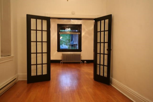 spare room featuring baseboard heating, radiator heating unit, hardwood / wood-style floors, and french doors