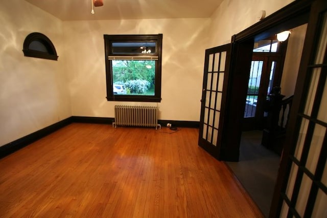 spare room with radiator heating unit, ceiling fan, french doors, and hardwood / wood-style floors