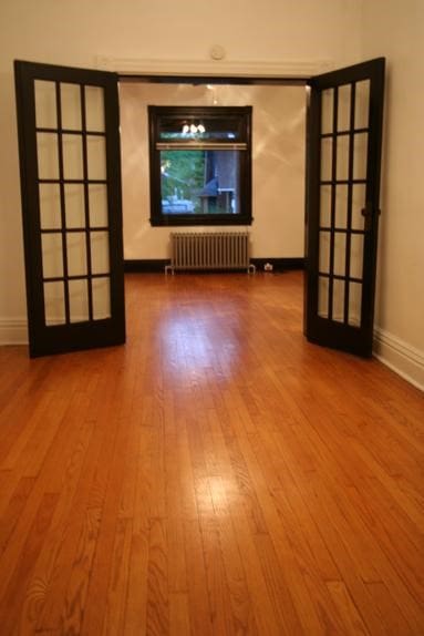 unfurnished living room featuring french doors, radiator, and hardwood / wood-style floors