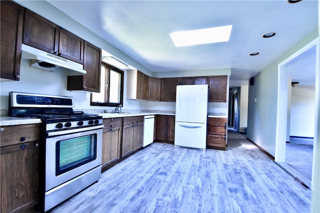 kitchen with white appliances, a skylight, light wood-type flooring, dark brown cabinetry, and sink