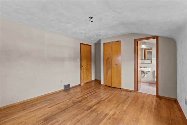 unfurnished bedroom featuring ensuite bath, sink, light hardwood / wood-style flooring, and vaulted ceiling