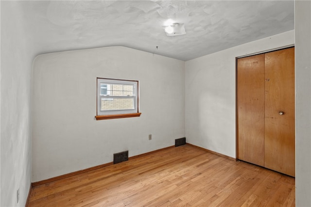 unfurnished bedroom with lofted ceiling, light hardwood / wood-style floors, and a closet