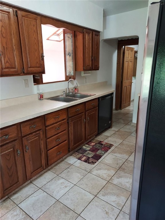 kitchen featuring black dishwasher, sink, stainless steel refrigerator, and light tile patterned floors