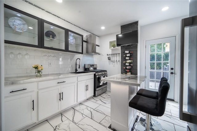 kitchen with a breakfast bar area, backsplash, gas range, wall chimney range hood, and sink