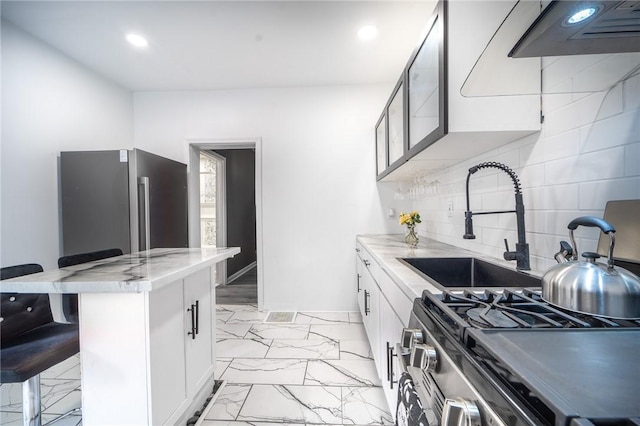 kitchen featuring range hood, a kitchen bar, decorative backsplash, white cabinetry, and stainless steel appliances