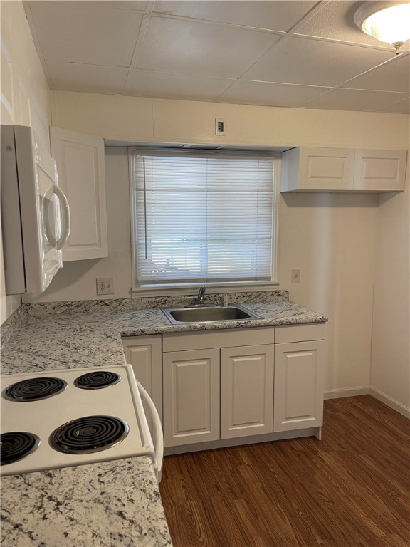 kitchen with white cabinets, dark hardwood / wood-style flooring, a paneled ceiling, stove, and sink