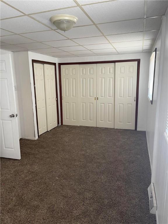 unfurnished bedroom with two closets, a paneled ceiling, and carpet