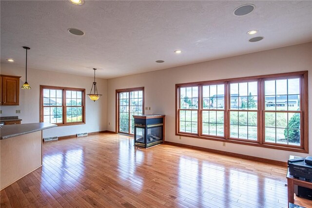 unfurnished living room featuring a healthy amount of sunlight, light hardwood / wood-style floors, and a textured ceiling