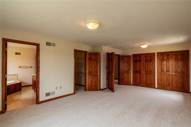 unfurnished bedroom featuring two closets, ensuite bathroom, and light colored carpet