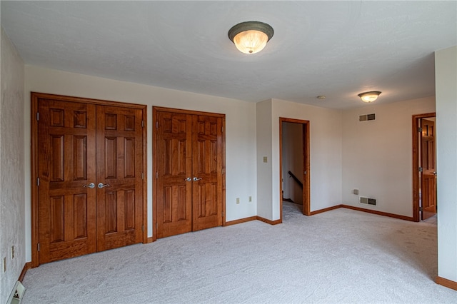 unfurnished bedroom with multiple closets and light colored carpet