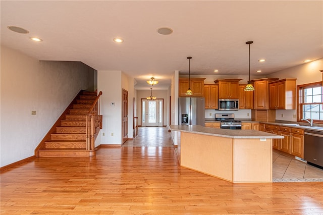 kitchen featuring light wood-type flooring, a center island, hanging light fixtures, appliances with stainless steel finishes, and sink