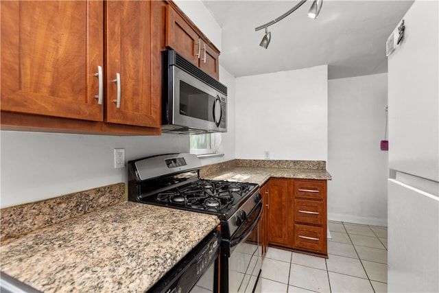 kitchen with light tile patterned flooring, white fridge, light stone countertops, track lighting, and range with gas stovetop