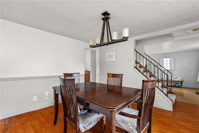 dining area with a textured ceiling, an inviting chandelier, and hardwood / wood-style flooring