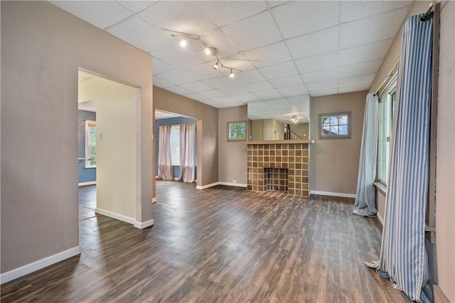 unfurnished living room with a fireplace, rail lighting, dark wood-type flooring, and a paneled ceiling