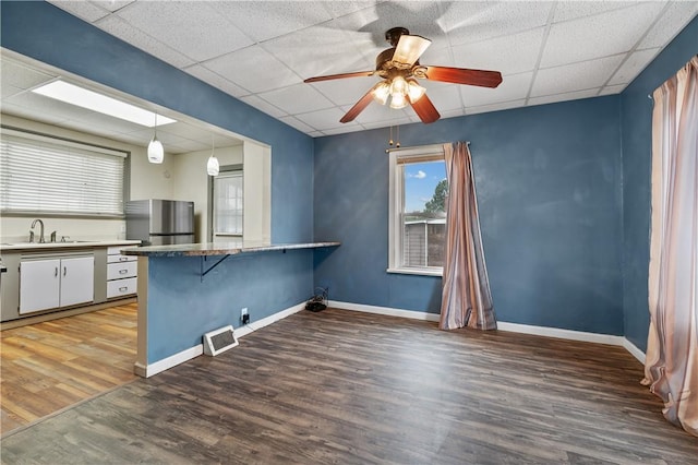 kitchen with a drop ceiling, hardwood / wood-style flooring, hanging light fixtures, white cabinets, and stainless steel refrigerator