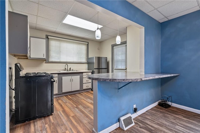 kitchen featuring a paneled ceiling, wood-type flooring, hanging light fixtures, and black range with gas cooktop