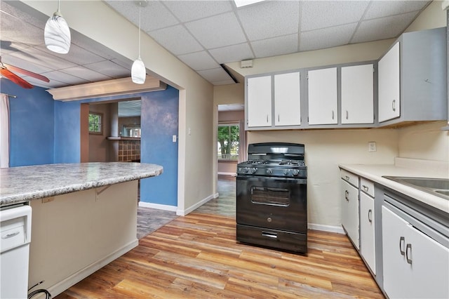 kitchen featuring a drop ceiling, ceiling fan, hanging light fixtures, black gas range oven, and light hardwood / wood-style floors