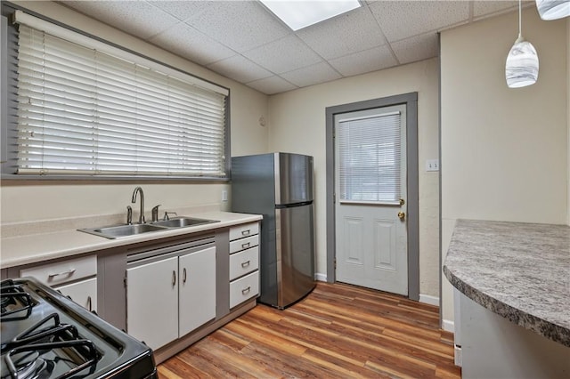 kitchen with sink, stainless steel refrigerator, hanging light fixtures, a drop ceiling, and wood-type flooring