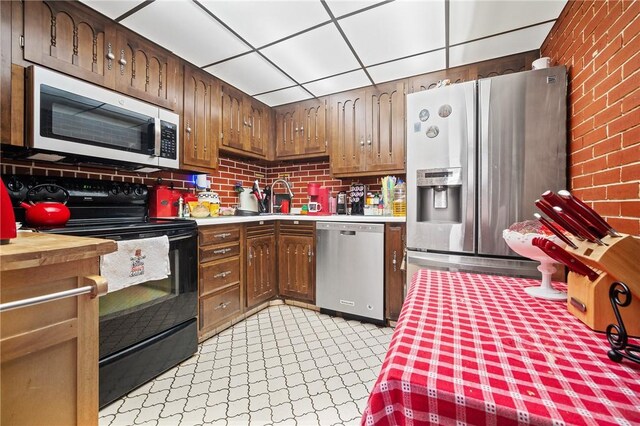 kitchen with sink, brick wall, stainless steel appliances, and light tile patterned floors