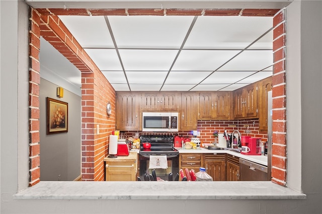 kitchen featuring sink, brick wall, appliances with stainless steel finishes, and light stone counters