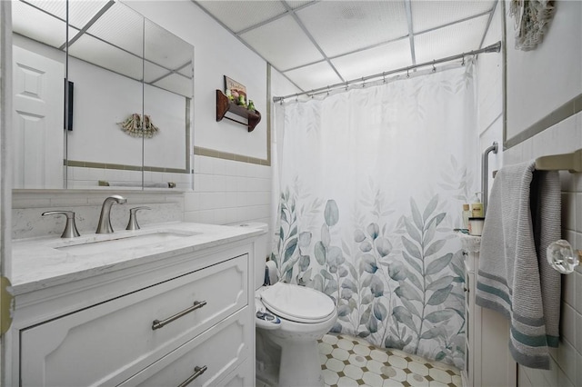 bathroom with a drop ceiling, tile walls, vanity, toilet, and a shower with shower curtain