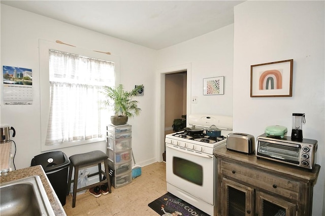 kitchen with white gas range, dark brown cabinets, and sink