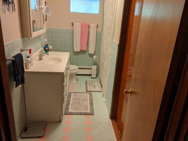 bathroom featuring a baseboard heating unit, toilet, vanity, tile walls, and tile patterned floors