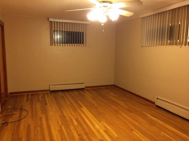 empty room with ceiling fan, baseboard heating, and wood-type flooring