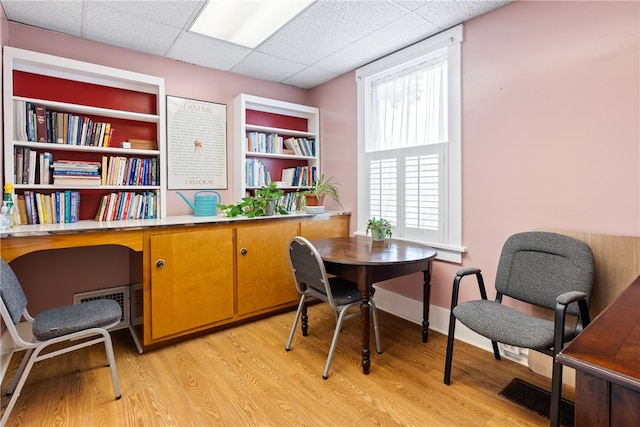 home office with built in shelves, a wealth of natural light, light wood-type flooring, and a paneled ceiling