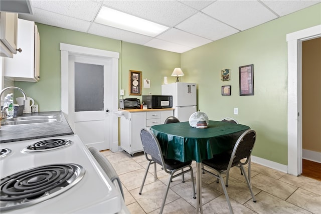 kitchen with light tile patterned flooring, white cabinets, a paneled ceiling, white refrigerator, and sink