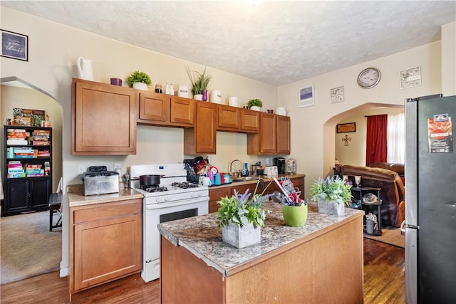 kitchen with gas range gas stove, stainless steel fridge, dark carpet, a textured ceiling, and a center island