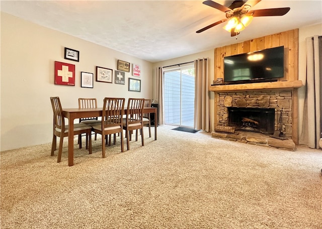 dining room featuring a stone fireplace, carpet, and ceiling fan