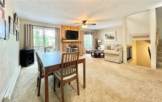 dining room with a stone fireplace, light carpet, and ceiling fan