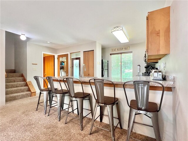 kitchen with kitchen peninsula, fridge, a kitchen bar, and light colored carpet