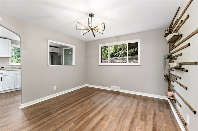 spare room featuring a wealth of natural light, a chandelier, and dark hardwood / wood-style flooring